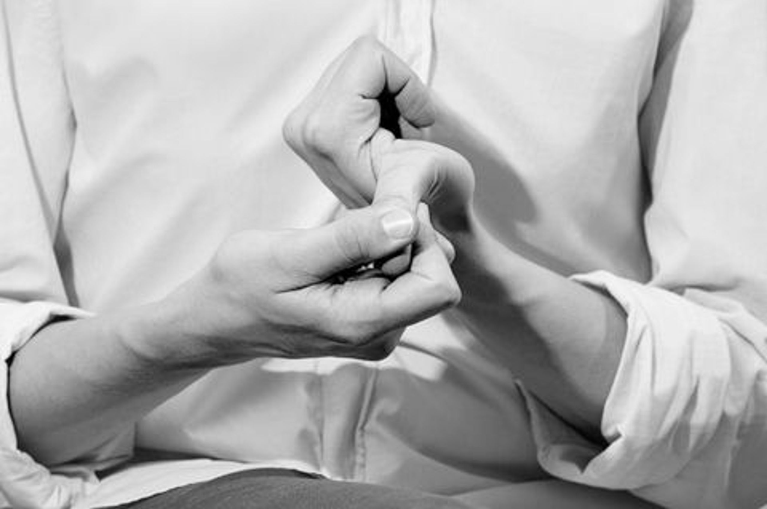 Two hands, one bending the other hand's thumb back and down toward the camera. The person is wearing a white button-up shirt.