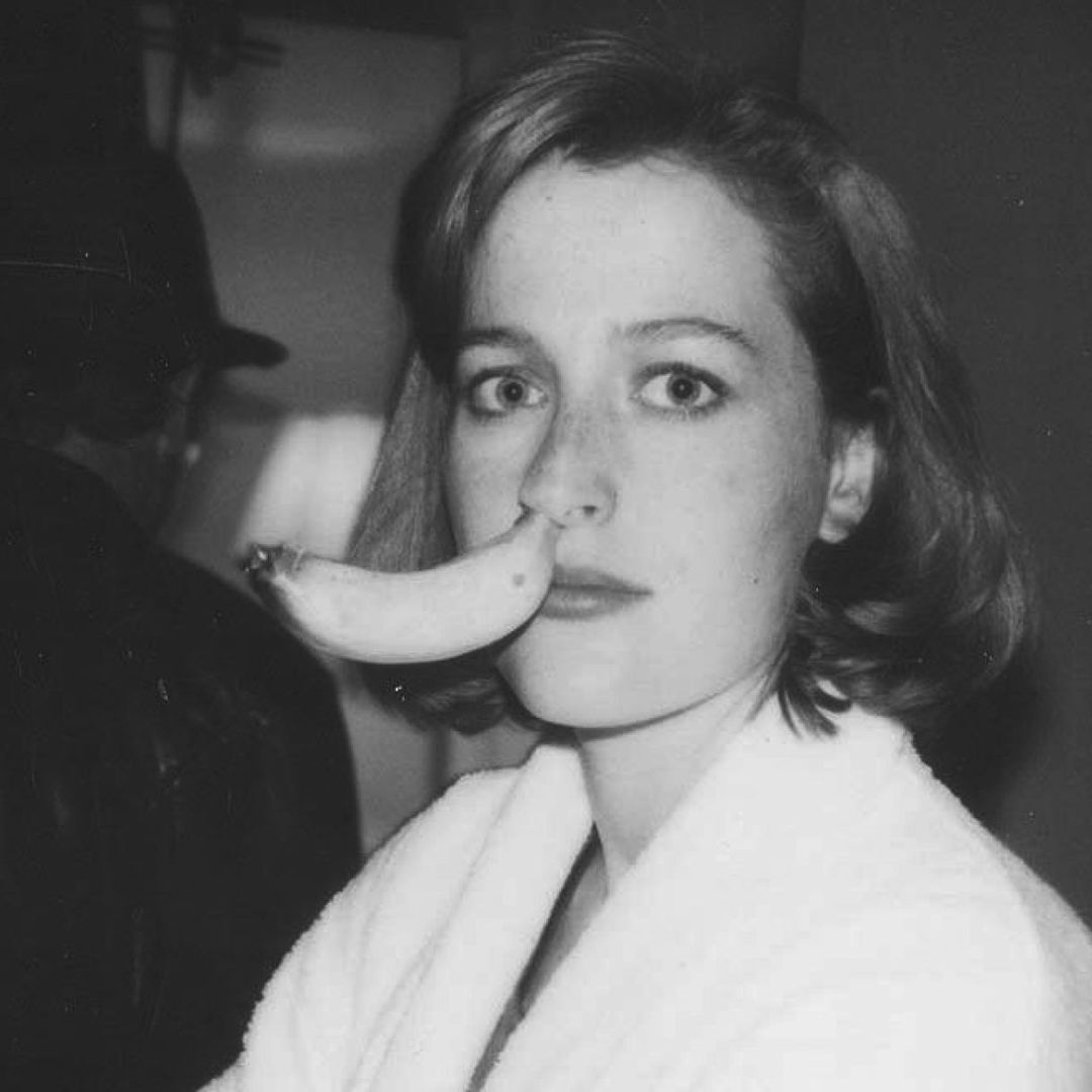 Black and white flash photo of a young Gillian Anderson with a banana stem up her nose.