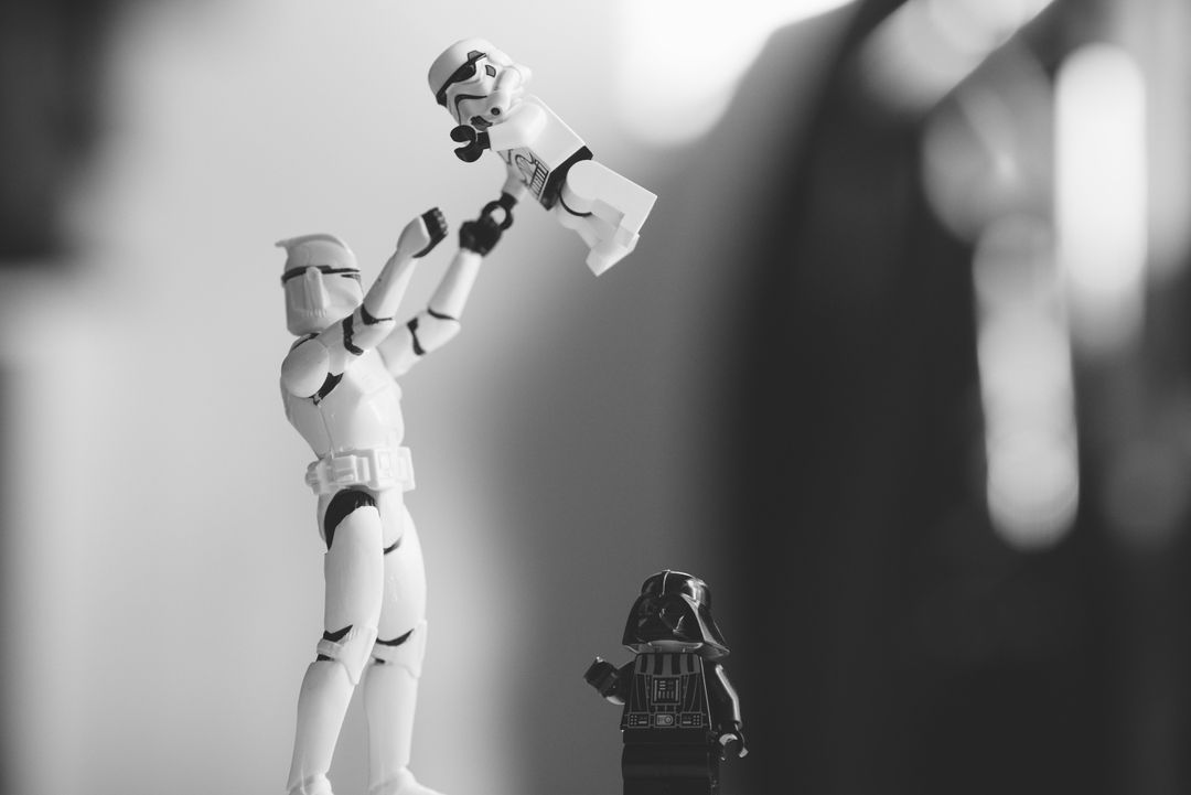 Monochrome Star Wars toys, an action figure father holding up a lego "son" with lego Darth Vader in the background. Photo by Daniel Cheung