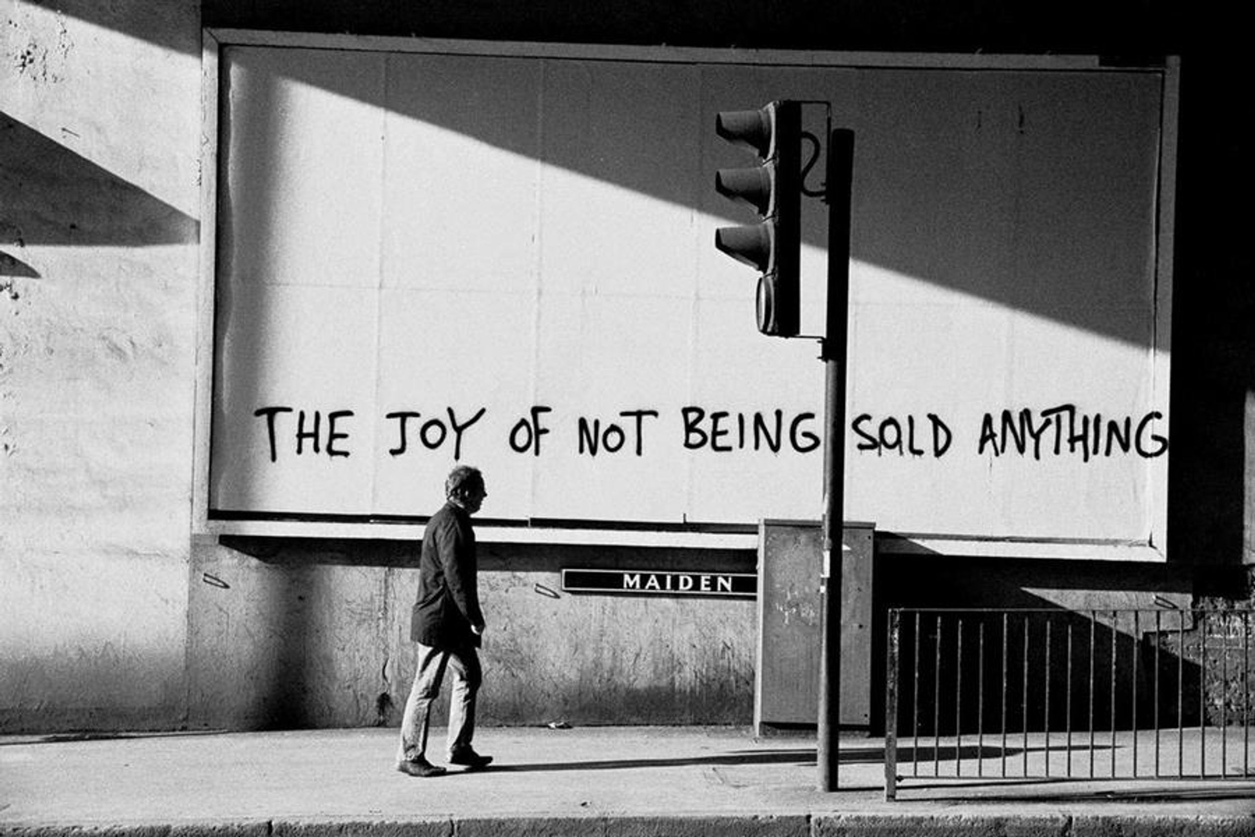 A person walking along a footpath. Spray painted onto the wall beside them: "THE JOY OF NOT BEING SOLD ANYTHING".